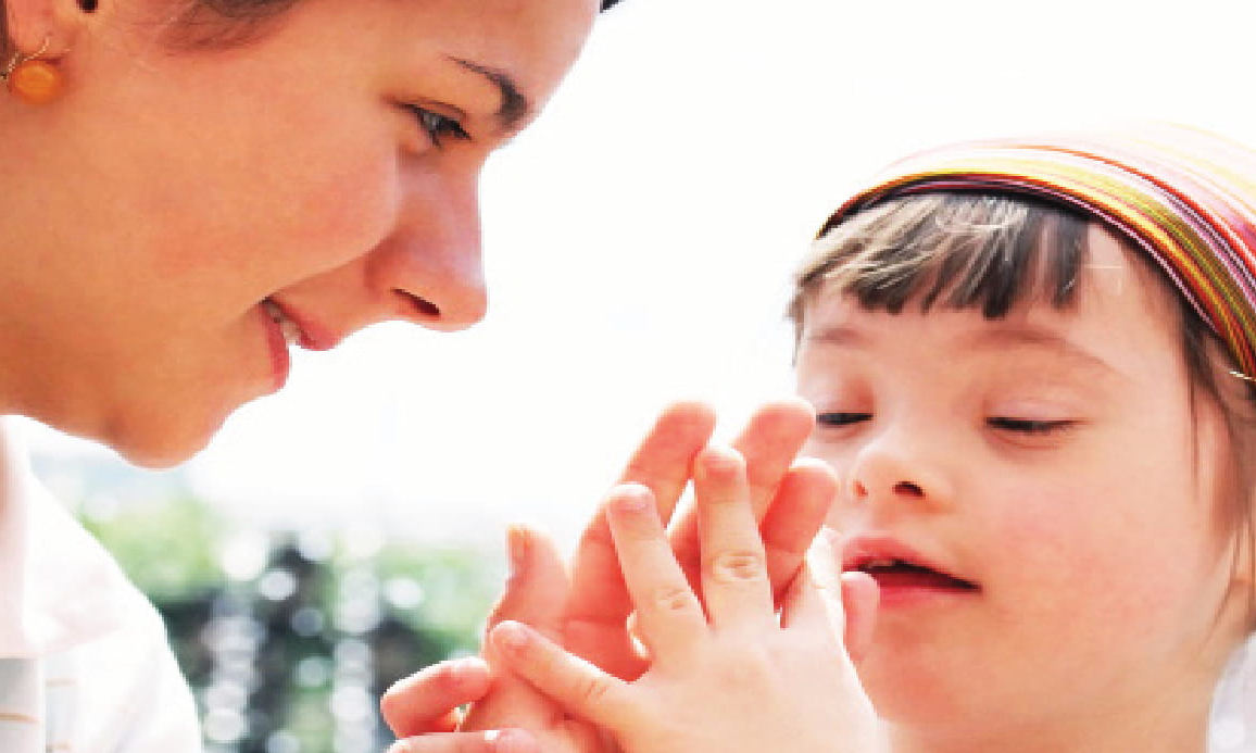 girl holding her hands together in front of her face with an adult next to her.
