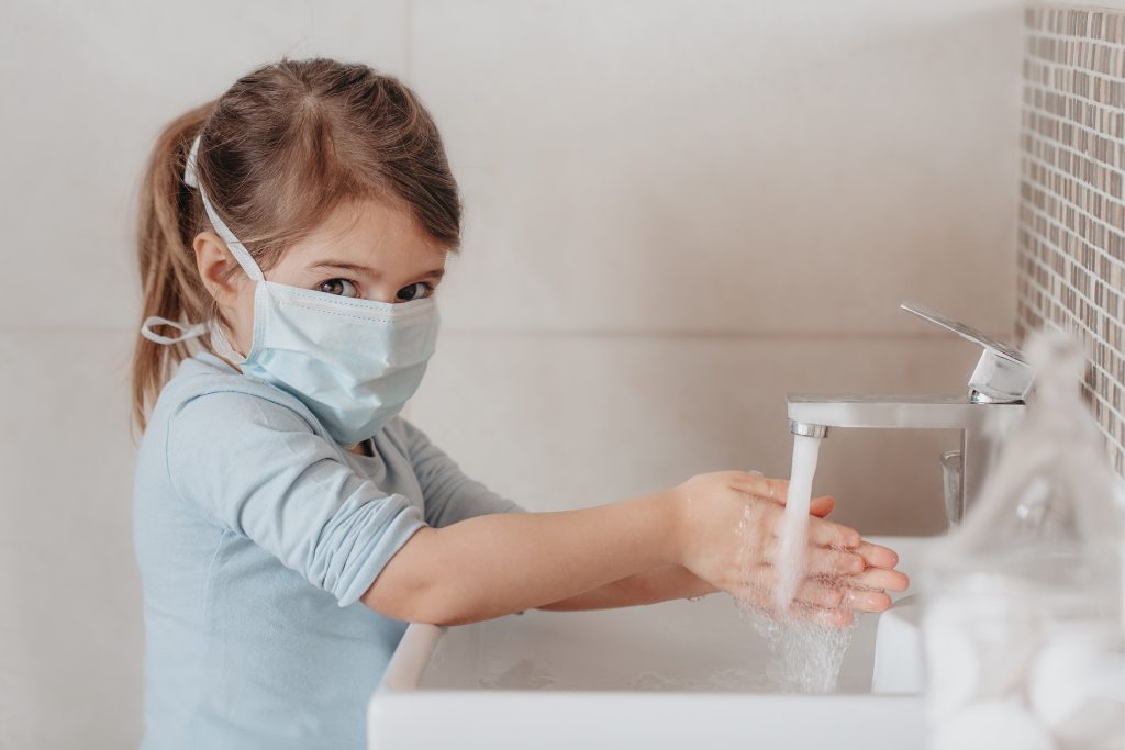 little girl wearing mask washing hands